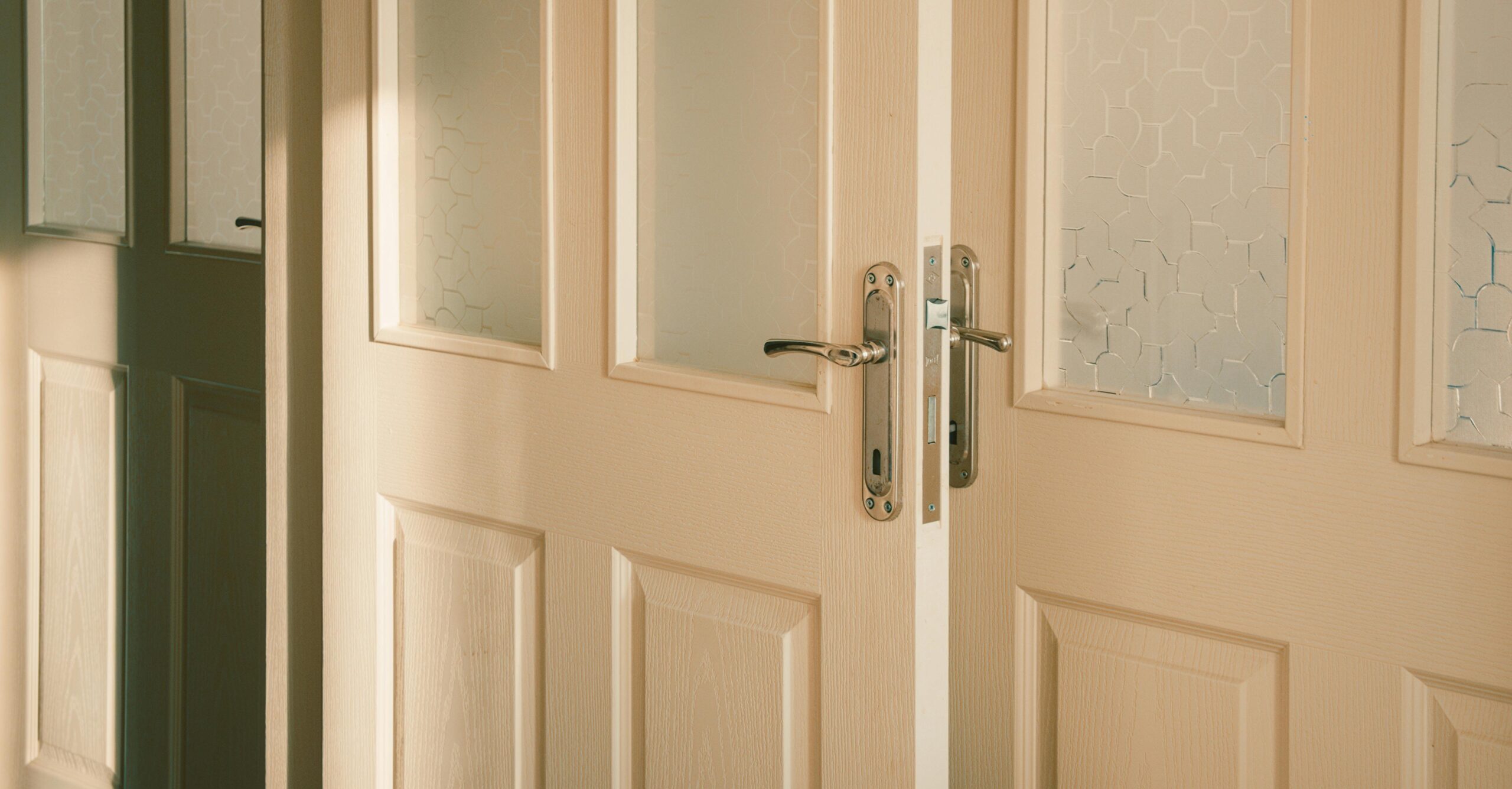 Light wood double interior doors with frosted glass panels and brushed silver lever handles